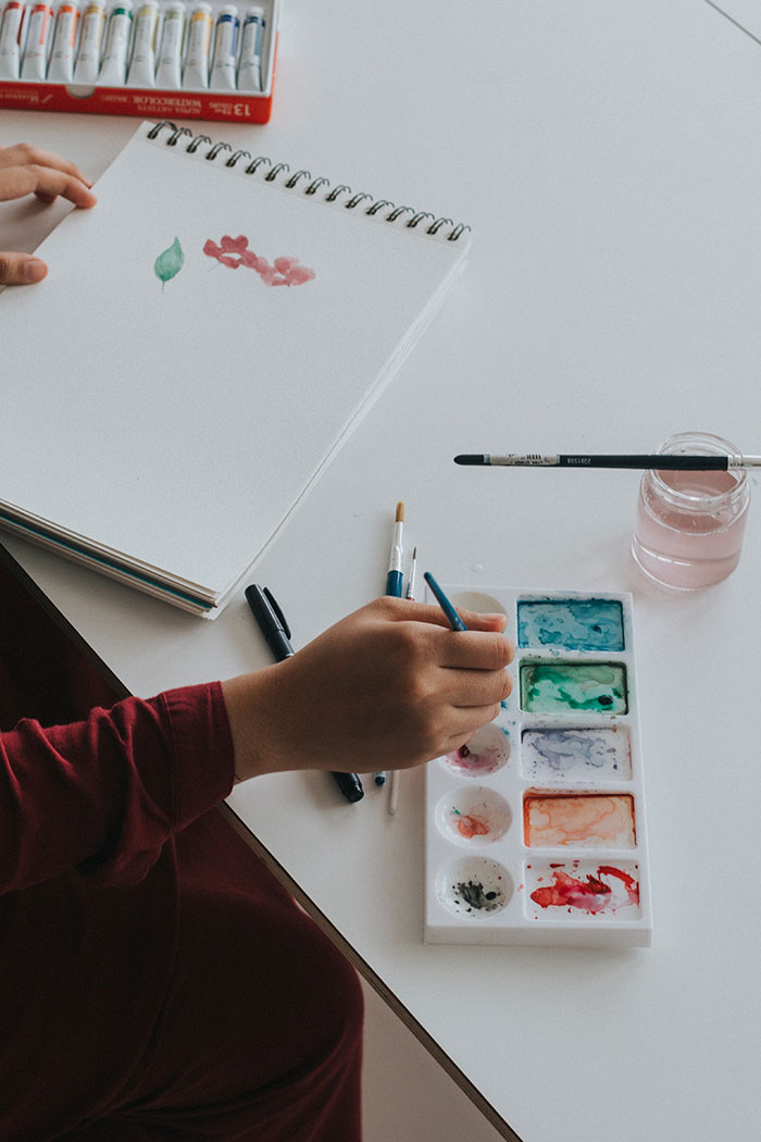Person enjoying painting alone with watercolors and sketchbook, practicing a relaxing solo activity.