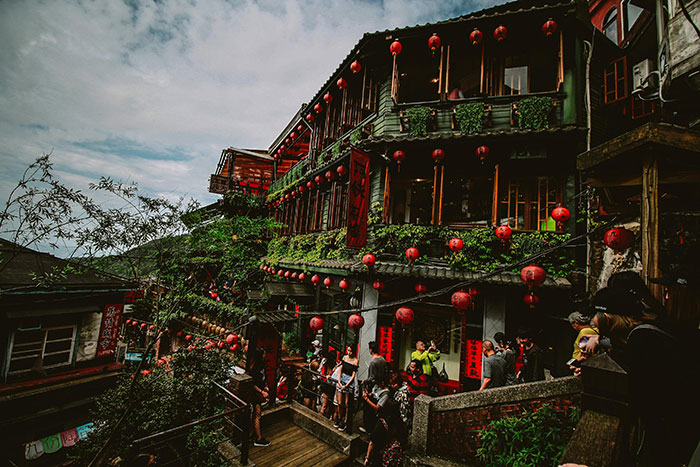 Traditional Asian building decorated with red lanterns and travelers exploring, showcasing friendly and welcoming nations.