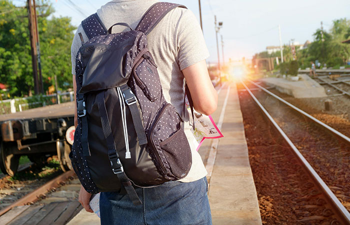 Traveler with backpack standing on train platform at sunset, exploring world travelers ranking friendliest and unwelcoming nations.