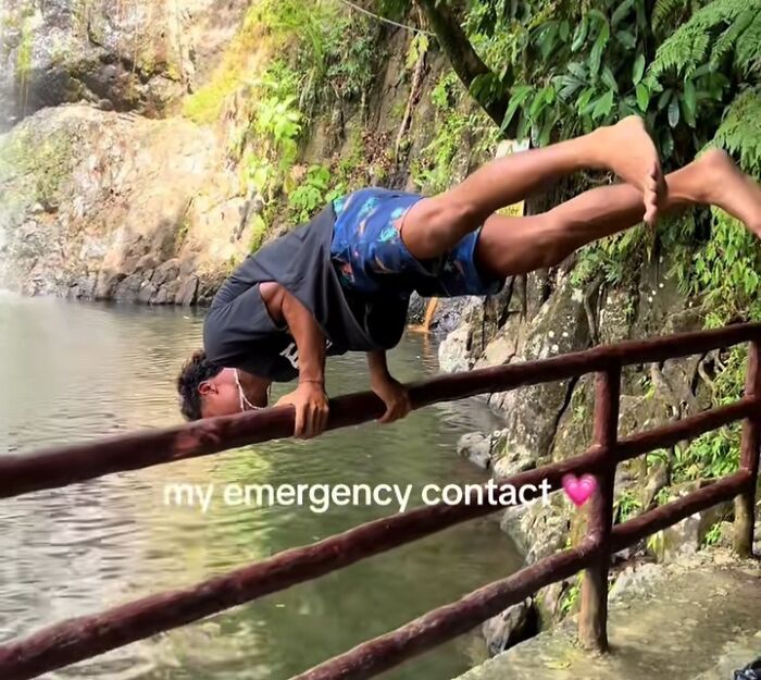 Man balancing precariously on a railing by a river, with "my emergency contact" text overlay.