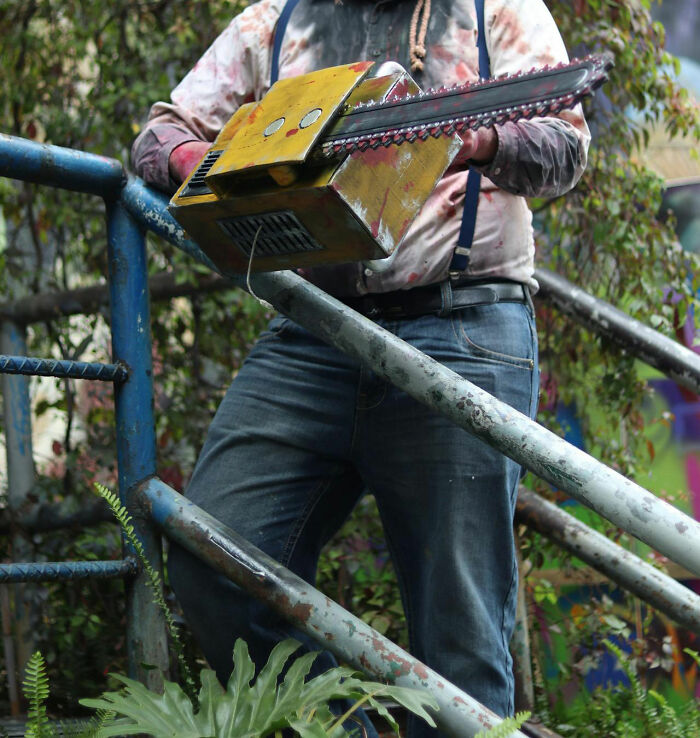 Hombre sosteniendo una motosierra, ilustrando un terror real al aire libre en un parque.