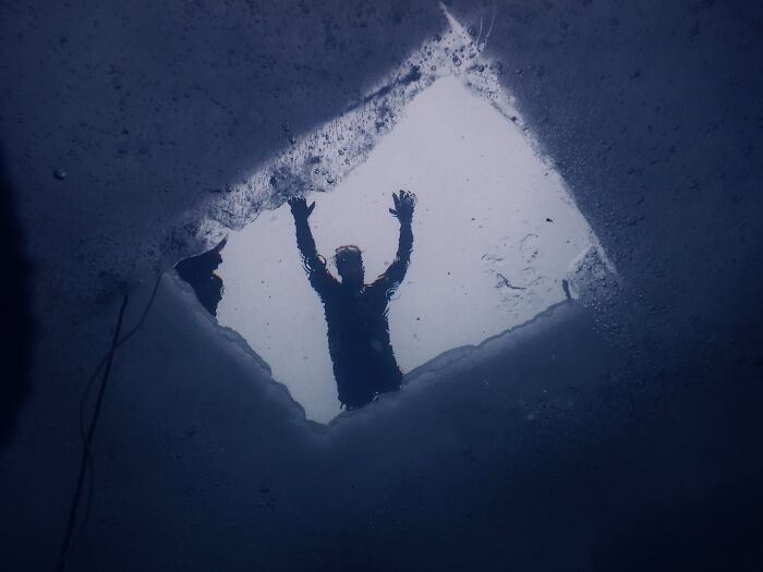 Persona reflejada en el agua, con las manos levantadas, enfrentándose a un terror real bajo la superficie helada.