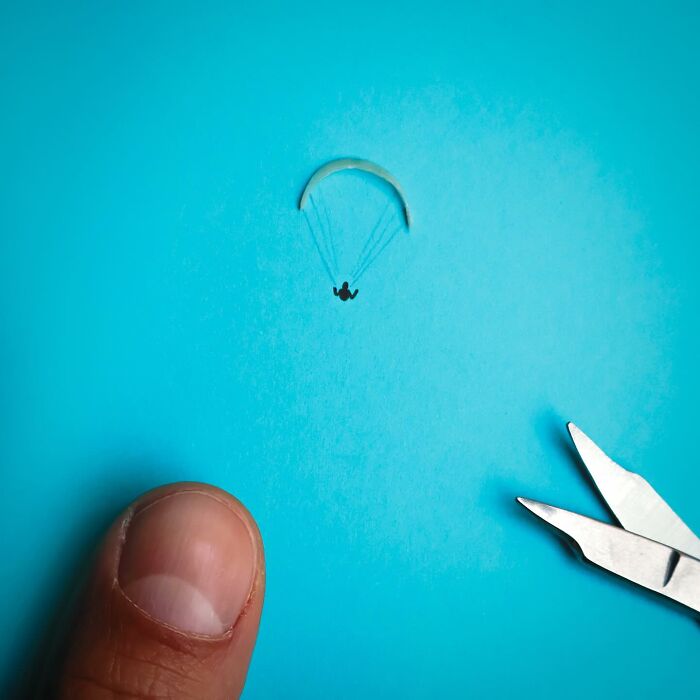 Playful illustration by Romain Joly featuring a tiny parachuter drawn beneath a pasted lens on blue paper.