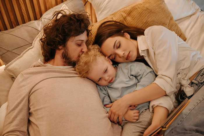 Couple napping with baby on bed, emphasizing peaceful family time during nap without unexpected visits.