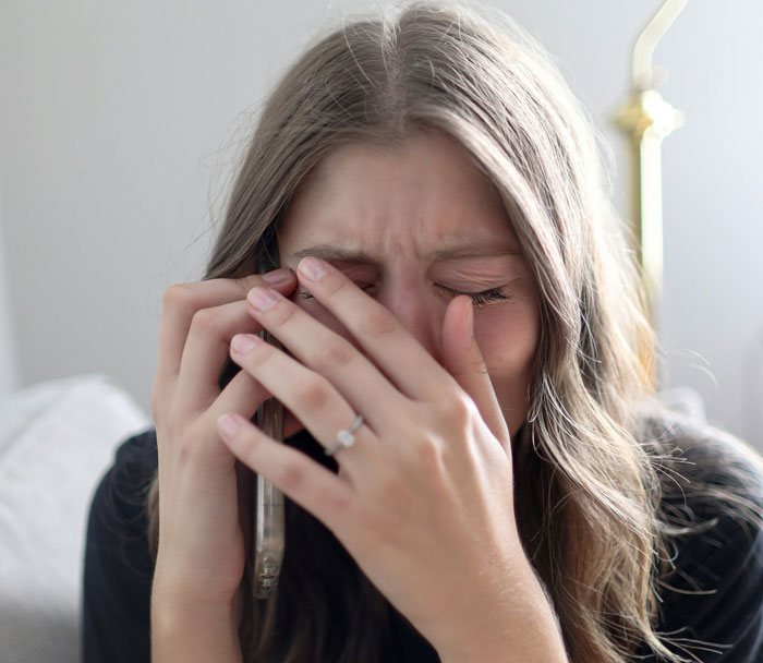 Woman covering face in distress while holding phone, illustrating conflict over obese mom babysitting newborn topic.
