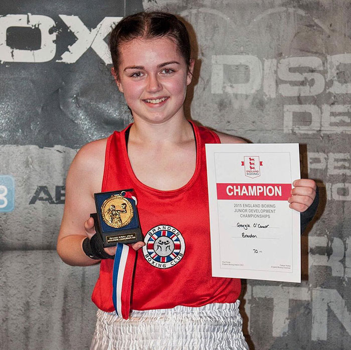 Young pro boxer Georgia O’Connor holding champion plaque and certificate at a boxing event.