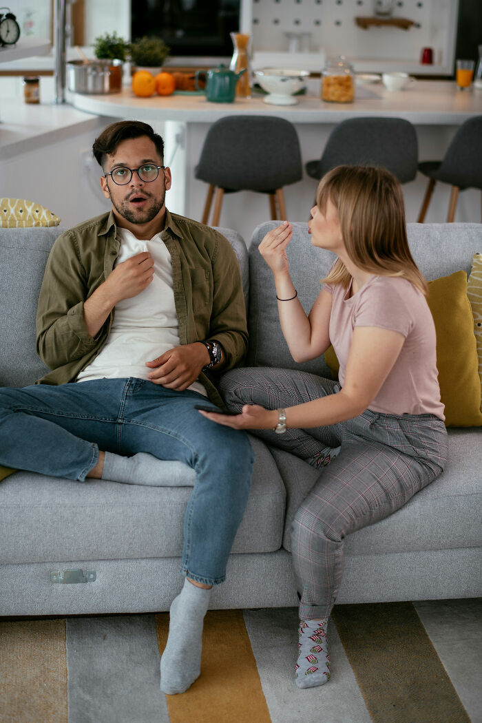 Man looking shocked while woman gestures in frustration on a couch, illustrating turn offs men want women to know.