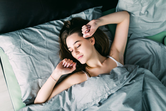 Young woman sleeping peacefully in bed under gray blankets in a calm bedroom setting at night.