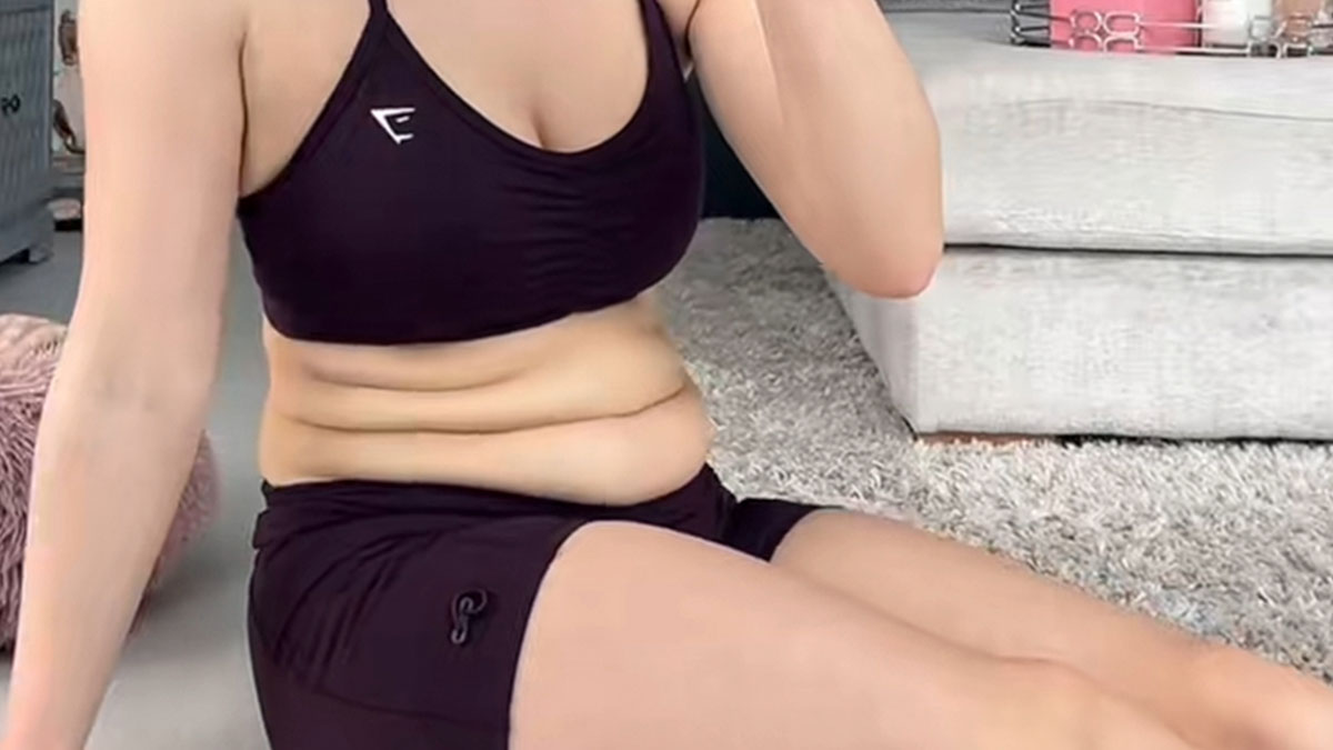 Woman wearing black workout clothes sitting on the floor showing unedited body and natural skin folds.
