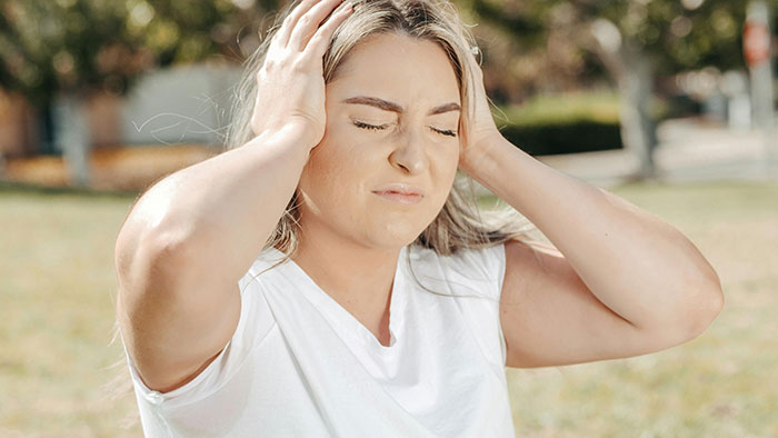 Woman holding her head in frustration outdoors, illustrating sibling conflict over refusing to turn home into shelter.