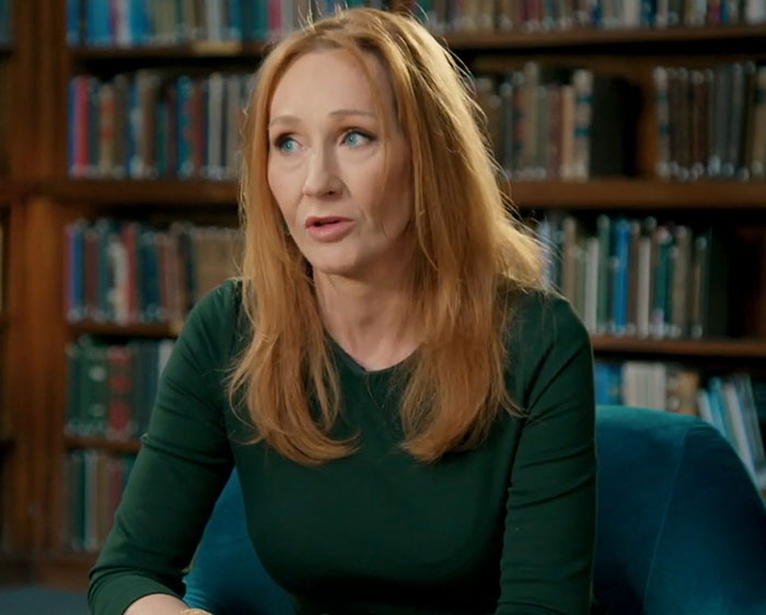 Author J.K. Rowling seated in a library speaking during an interview about Harry Potter fans and Tom Felton comments.
